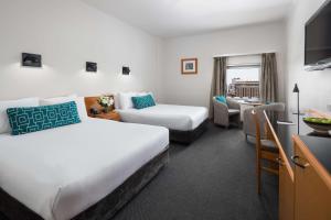 a hotel room with two beds and a desk at Rydges Darwin Central in Darwin