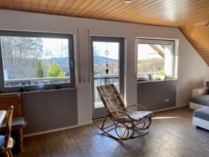 een woonkamer met 2 ramen en een schommelstoel bij Ferienwohnung mit Ausblick in Mömbris