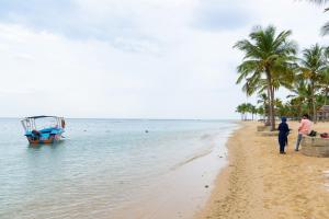 two people standing on a beach with a boat in the water at Gnanam Holiday Inn in Pasikuda