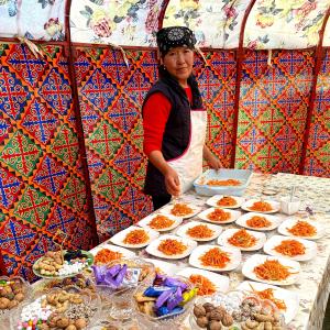 a woman standing in front of a table of food at Yurt camp ALI-NUR at lake Song-Kol юрточный лагерь Али-Нур озеро Сон-Куль Сон-Куль Кыргызстан Нарын Kyrgyzstan Naryn in Naryn