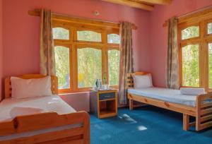 two beds in a room with pink walls and windows at Maney Homestay - Thiksey - Leh in Ranbirpura