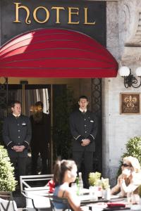 dos hombres de uniforme de pie bajo un paraguas rojo en Hôtel de la Cigogne en Ginebra