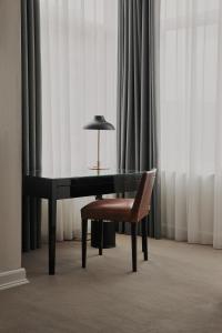 a desk and a chair with a lamp and curtains at Avenue Hotel Copenhagen by Brøchner Hotels in Copenhagen