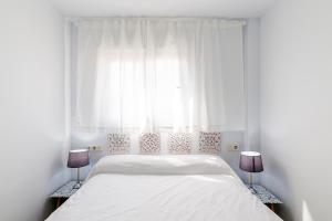 a white bedroom with a bed and two lamps at Apartamentos “Mar de Coral” Aguadulce in Aguadulce