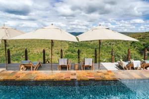 a swimming pool with two umbrellas and chairs and a table and chairsktop at Rhino Ridge Safari Lodge in KwaNompondo