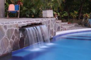a pool with a waterfall next to a stone wall at Lote 44 Guesthouse in El Zonte