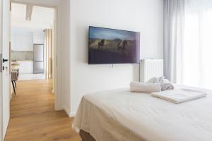 a white bedroom with a bed and a tv on the wall at New modern style home next to the train station in Thessaloniki