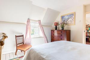 a bedroom with a bed and a chair and a window at Thatched Hat Cottage in Lymington