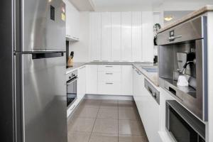 cocina con armarios blancos y nevera de acero inoxidable en Pool View City Centre Apartment 202 en Cairns