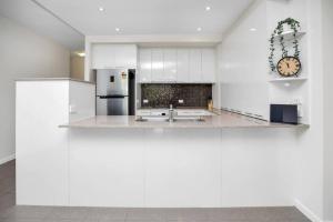 a kitchen with white cabinets and a clock on the wall at Pool View City Centre Apartment 202 in Cairns