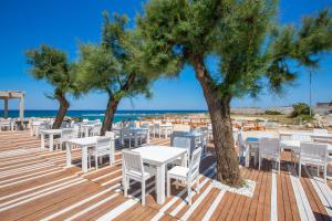 una terraza de madera con mesas blancas y sillas en la playa en La vista mare da Rossella, en Specchiolla