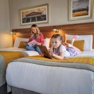 une petite fille assise sur deux lits avec un ordinateur portable dans l'établissement Maldron Hotel Derry, à Derry Londonderry