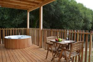 una terraza de madera con bañera de hidromasaje, mesa y sillas en Cabañas Compostela - Cabaña A Fervenza, en Santiago de Compostela