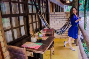 a woman in a blue dress standing next to a table with a wine glass at Chalé 03 Itaipu Vale da Colina Niterói in Niterói