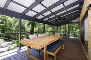 un patio con una mesa de madera y sillas en una terraza en Rainforest River Retreat Kangaroo Valley, en Upper Kangaroo River