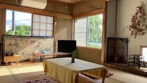 a living room with a table and a tv and windows at ゲストハウス蘖 -ひこばえ in Kitakami