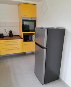 a kitchen with a stainless steel refrigerator and yellow cabinets at Logement Campagne Coquelicots Plaisance in Le Lamentin
