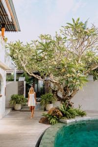 a woman walking past a tree next to a swimming pool at Ecozy Dijiwa Canggu in Canggu
