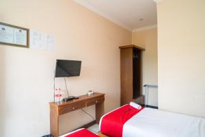 een slaapkamer met een bed en een bureau met een televisie bij RedDoorz Plus Syariah At Lotus Hotel Bojonegoro in Bojonegoro