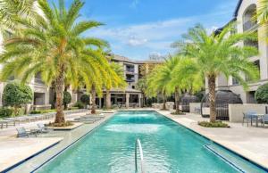 a swimming pool with palm trees in front of a building at Lovely Texas Medical Center 1 Bedroom Luxury Suite in Houston