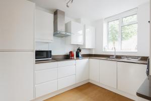 ロンドンにあるBright & welcoming garden flat sleeps 6 in styleの白いキャビネットと窓付きの白いキッチン