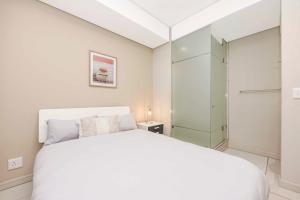 a bedroom with a white bed and a glass closet at Tyrwhitt Luxury Apartment in Rosebank - with generator in Johannesburg