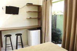 a bedroom with two bar stools and a tv and a window at Sun Suítes in Ubatuba