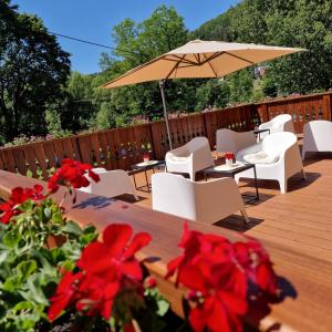 a deck with white chairs and an umbrella and red flowers at Willa jak u Babci in Wisła