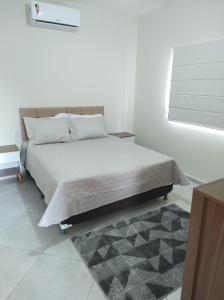 Una cama en un dormitorio blanco con una alfombra. en Apartamento mobiliado com vista exclusiva da Serra, en Cruzeiro
