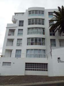 un bâtiment blanc avec un palmier en face dans l'établissement Lovely 2 bedroom self-catering apartment located 1 min from the beach, à Strand