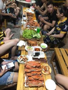 eine Gruppe von Menschen, die an einem langen Tisch mit Essen sitzen in der Unterkunft Nhat Ha Homestay in Vũng Tàu