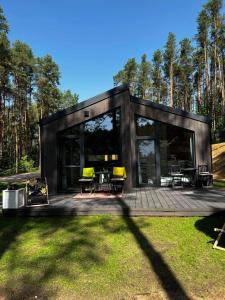 a small black house with a deck with yellow chairs at Brama do lasu - Domek Relaksu in Borków