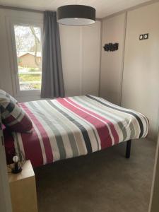 1 cama con manta a rayas en una habitación con ventana en Chalet, en Labouheyre