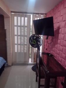 Habitación con pared de color rosa y escritorio con TV. en APARTAMENTO PARA TRES PERSONAS a 10 minutos del centro de eventos valle del pacifico y a la misma distancia del centro de la ciudad Y también a 300 mts del Orquideorama en Cali