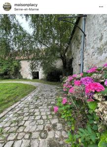 a stone pathway with pink flowers next to a building at Grande ferme à 50min de Paris in Le Plessis-Placy