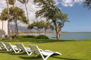 una fila di sedie bianche sedute sull'erba vicino all'acqua di Maui Beach Hotel a Kahului