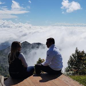 un homme et une femme assis au sommet d'une montagne avec des nuages dans l'établissement Mirante 45 - O Chalé mais alto do Brasil, localizado a 24km de Campos do Jordão, à Santo Antônio do Pinhal