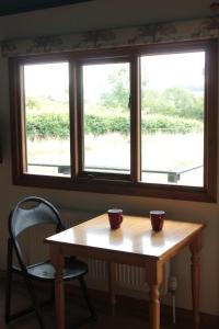 two cups on a wooden table in front of a window at Couples Camping Cabin in Ashbourne