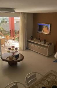 ein Wohnzimmer mit einem TV und einem Tisch in der Unterkunft Areias de Itacimirim 104 Village - Pé na Areia in Itacimirim