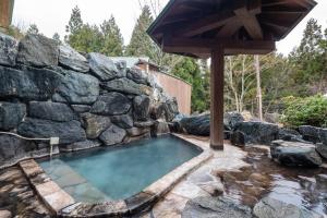 uma piscina com uma parede de pedra e um guarda-sol em 田沢湖水沢温泉郷セルリアンリゾートAoni em Senboku
