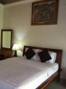 1 dormitorio con cama blanca y almohadas negras en Raka Rai Bungalows en Ubud
