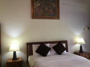 1 dormitorio con 1 cama con 2 lámparas y una pintura en la pared en Raka Rai Bungalows, en Ubud