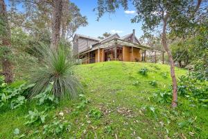 a house sitting on top of a grassy hill at Goanna Cottage - Woodstone Estate in Dunsborough