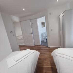 a white bedroom with two beds and a bathroom at Modern home with Netflix, NowTV & 2private parking in East Tilbury