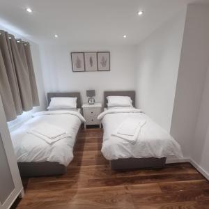 Habitación con 2 camas individuales y suelo de madera. en Modern home with Netflix, NowTV & 2private parking en East Tilbury