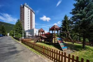 einen Spielplatz neben einem Zaun mit einem Gebäude in der Unterkunft Hotel Horizont in Pec pod Sněžkou