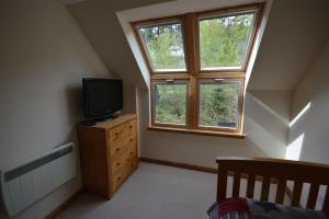 a bedroom with a tv on a dresser and two windows at Tall Pines Apartment in Spean Bridge