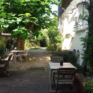 eine Terrasse mit einem Tisch, Stühlen und einem Baum in der Unterkunft Les Charmilles in Saint-Jean-de-Losne