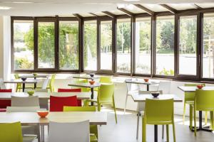 a dining room with tables and chairs with windows at ibis Styles Niort Poitou Charentes in Vouillé