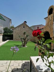 a garden with red flowers and a stone building at Apartments Šime in Šibenik